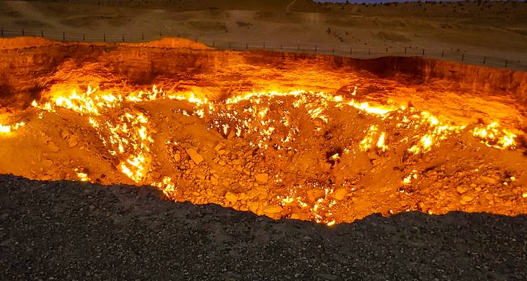 Cráter de gas ardiente brillando en naranja en un paisaje desértico por la noche.