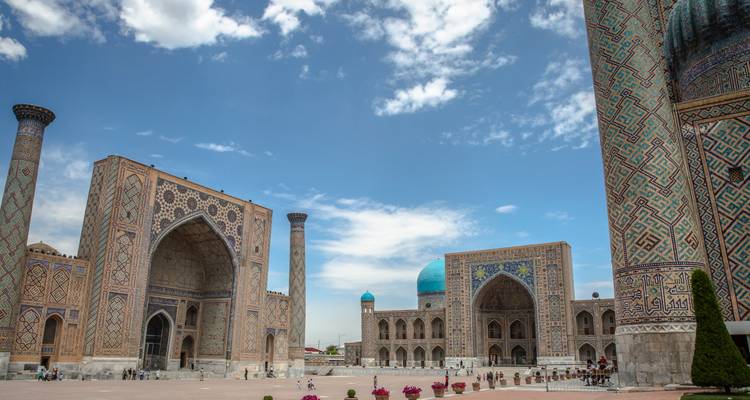 Grandes madrasas islámicas con cúpulas de color turquesa enmarcando una amplia plaza pública bajo un cielo azul.