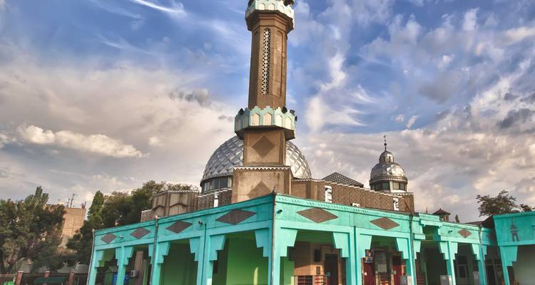 Colorida Mezquita Dungan de madera turquesa con un minarete distintivo recortado contra un cielo dramático lleno de nubes en Karakol.