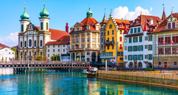 Paseo marítimo rico en colores de Lucerna con la Iglesia de los Jesuitas reflejada en aguas cristalinas y azul verdosas en un día soleado.