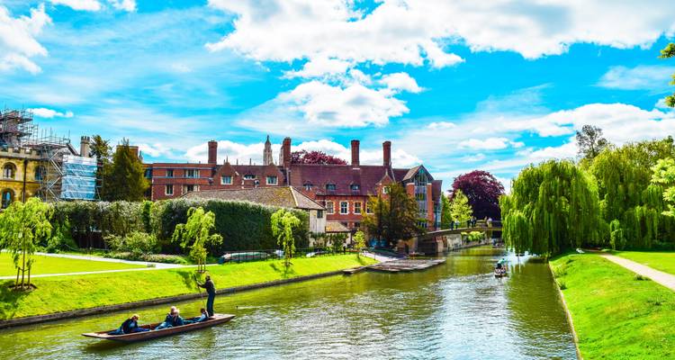 Colorful scene of punters steering wooden boats along the tranquil River Cam beside lush college gardens in Cambridge.