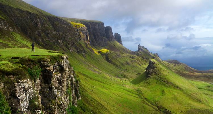 Dramatic green cliffs and ridges of a highland landscape with a lone hiker for scale