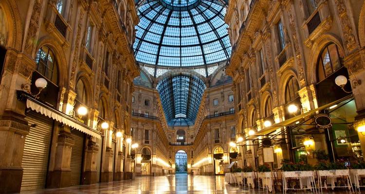 Interior elegante de la Galleria Vittorio Emanuele II con cúpula de cristal, arcos ornamentados y boutiques iluminadas.