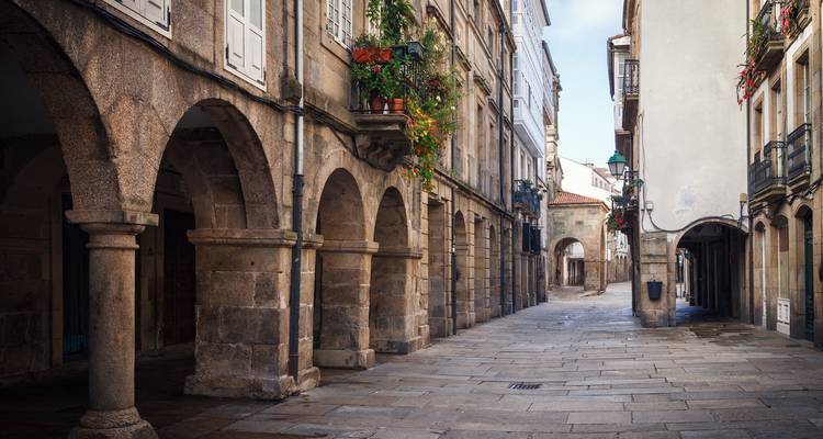 Mit Steinen gepflasterte Gasse, die von historischen Arkadenhäusern mit blumengeschmückten Balkonen in einer alten galizischen Stadt gesäumt wird.