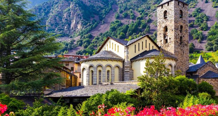 Église en pierre pittoresque avec abside arrondie dans une vallée de montagne verdoyante d'Andorre, encadrée par des fleurs éclatantes.