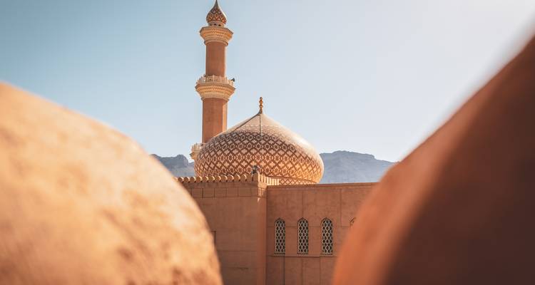 Cúpula decorativa y minarete de una mezquita enmarcados artísticamente entre muros de adobe bajo un cielo despejado.