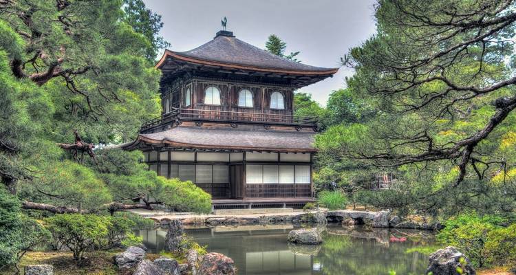 Traditioneller japanischer Tempel, umgeben von Bäumen und einem Teich.
