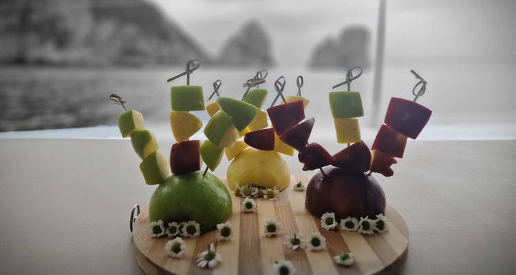 Brochetas de frutas coloridas arregladas creativamente con un fondo de mar difuminado.