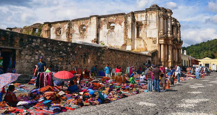 El colorido mercado textil se extiende a lo largo de la calle empedrada junto a las ruinas coloniales desgastadas.