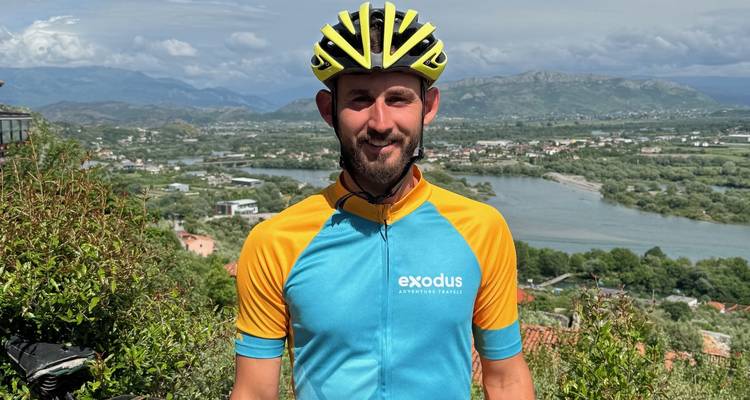 Portrait of a male cyclist in branded jersey with a panoramic valley and river behind him.