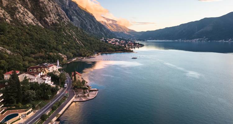 Zonsondergang uitzicht over de Baai van Kotor met kustplaatsjes, bergen en kalm weerspiegelend water.