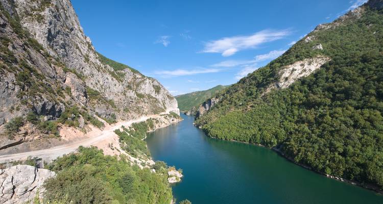 Steile rotsachtige kloof met smaragdgroene rivier die slingert tussen beboste rotswanden onder een strakblauwe hemel.
