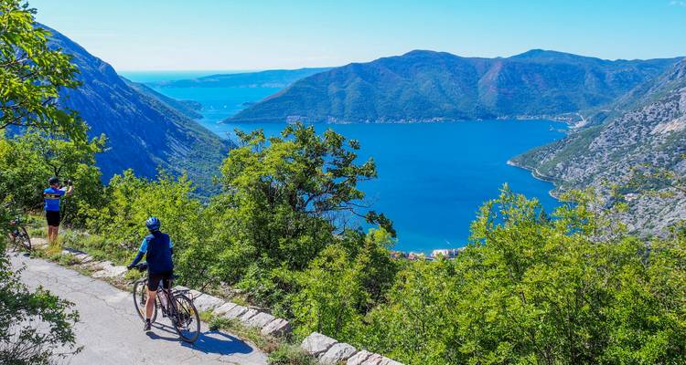 Les cyclistes font une pause sur une route de montagne côtière surplombant la baie de Kotor aux eaux bleu vif, encadrée par des pentes verdoyantes escarpées