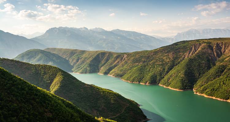 Vaste réservoir d'eau émeraude sinuant entre des crêtes couvertes d'arbres avec des montagnes lointaines brumeuses