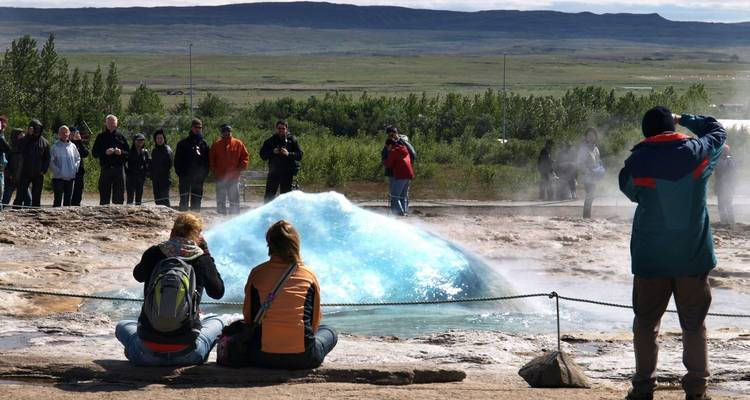 Personas observando un géiser hacer erupción con agua rociando en el aire.