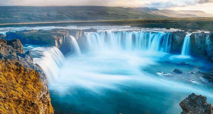 Impresionante cascada con un arcoíris en la neblina, situada en un paisaje escarpado.
