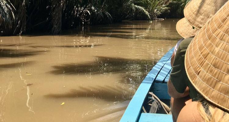 Personas con sombreros tradicionales navegando en un bote por un río lodoso.