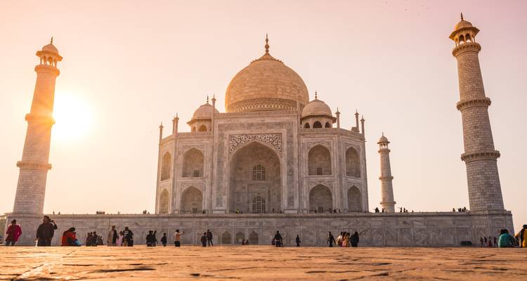 El Taj Mahal con gente alrededor, el sol poniéndose en el fondo.