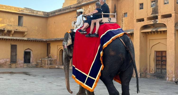 Una pareja pasea sobre un elefante decorado con coloridos paños dentro de las murallas históricas del fuerte.