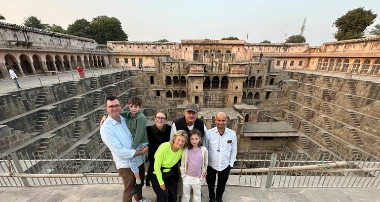 Un grupo familiar se para en la barandilla mirando hacia los dramáticos pisos del pozo escalonado de Chand Baori.