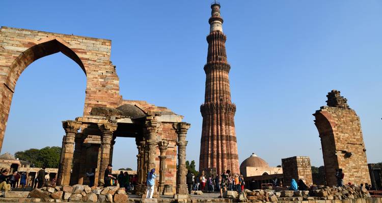Qutub Minar entouré de ruines et de touristes par une journée ensoleillée.