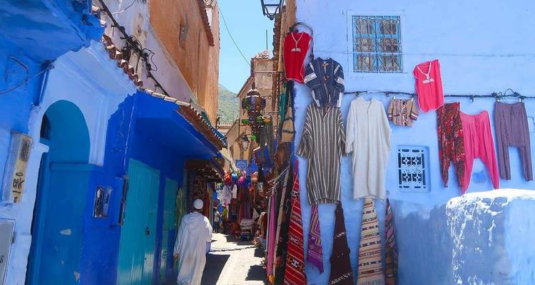 Blue alleyway with hanging clothes and a person in a robe walking away.
