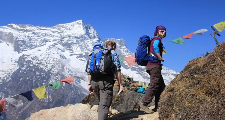 Dos excursionistas subiendo por un sendero con banderas de oración.