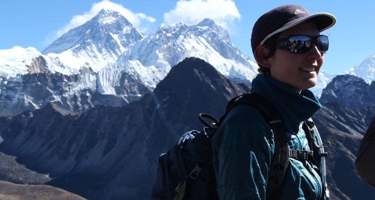 Persona con mochila posando frente a un pico de montaña.