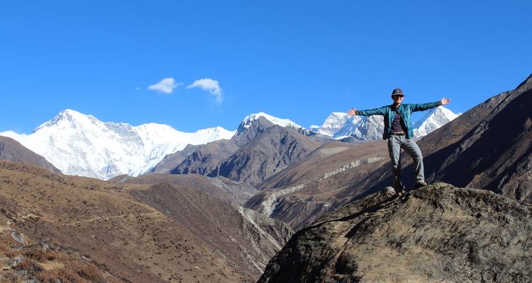 Excursionista en una cima montañosa con cielo despejado y montañas cubiertas de nieve.