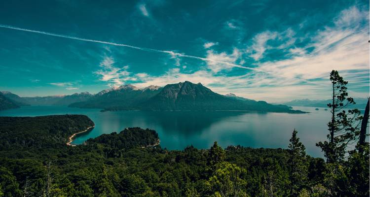 A wide view of a serene lake with mountains in the background under dramatic clouds.