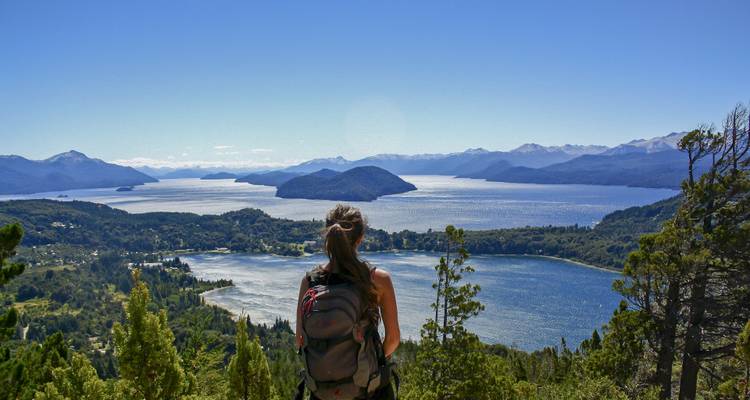 A person with a backpack overlooking a vast lake surrounded by mountains.