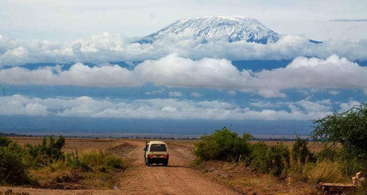 Un véhicule sur une route de terre menant vers une montagne avec des nuages.