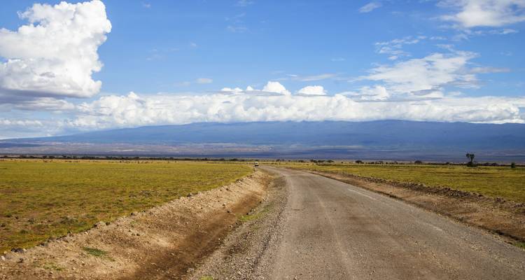 Chemin de terre à travers un vaste paysage ouvert avec des montagnes au loin.