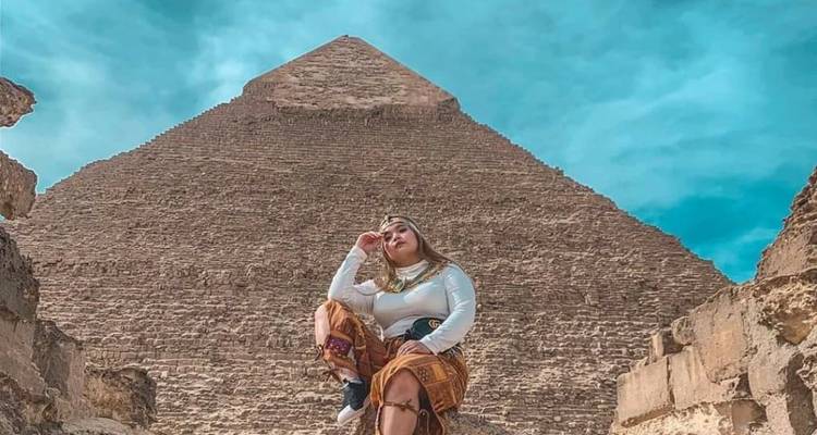 Persoon poseert voor een grote piramide onder een blauwe hemel.