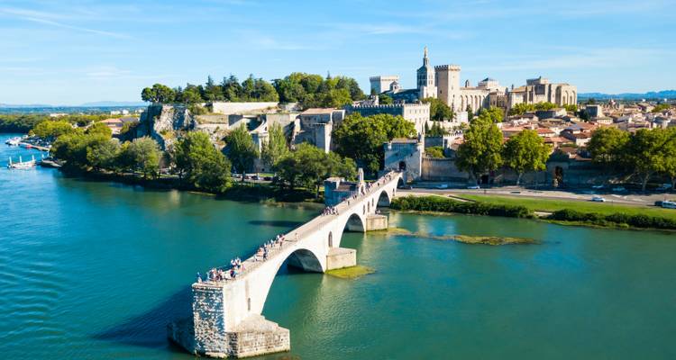 Famous stone Pont Saint-Bénézet bridge crossing the Rhône River with Avignon’s medieval skyline and Papal Palace in the background.
