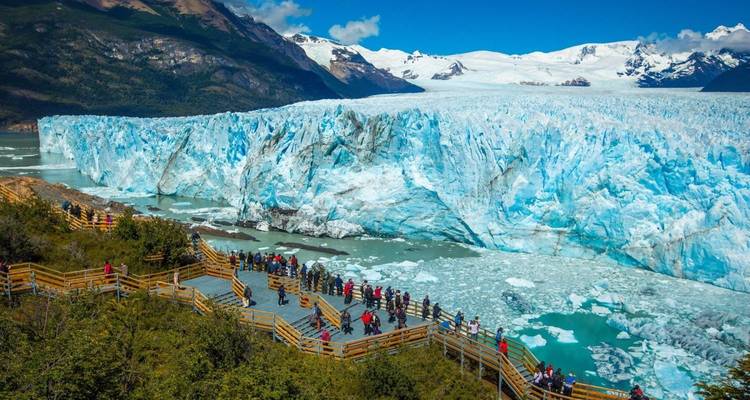Des touristes marchant sur un sentier en bois avec un glacier en arrière-plan.