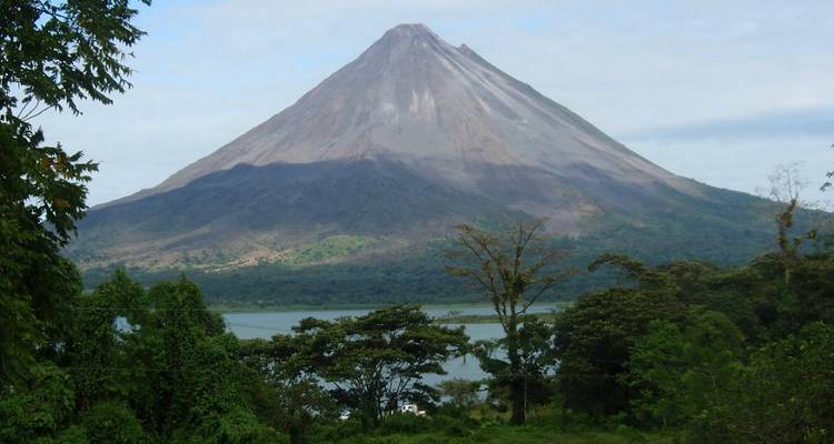 Volcán solitario con vegetación exuberante abajo y un lago.