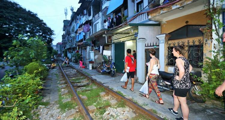 Menschen, die entlang eines Bahngleises inmitten städtischer Wohnbebauung gehen.
