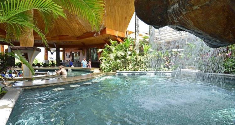 Ein Hallenbad-Bereich mit einem Wasserfall und tropischen Pflanzen.
