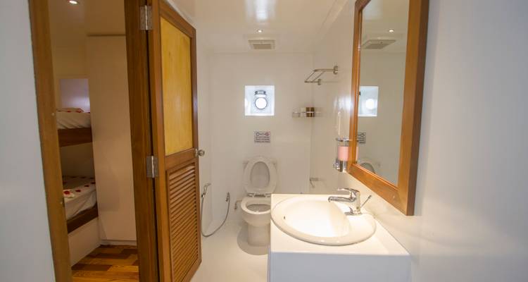 Salle de bain attenante immaculée avec lavabo, toilettes et douche à l'intérieur d'une cabine de bateau.