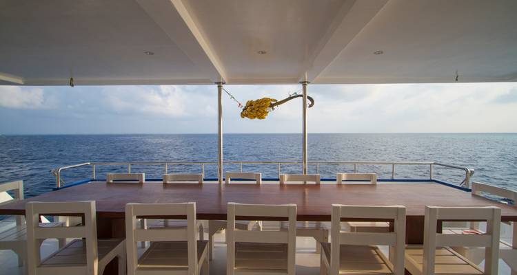 Table de salle à manger extérieure avec chaises blanches à la poupe d'un yacht donnant sur l'océan sans fin.