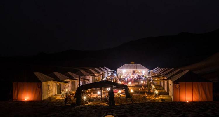 Zeltlager-Aufbau bei Nacht mit Lichtern in der Wüste.