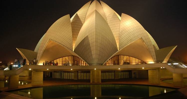 Night view of Lotus Temple glowing with warm internal lighting reflected in surrounding pools.