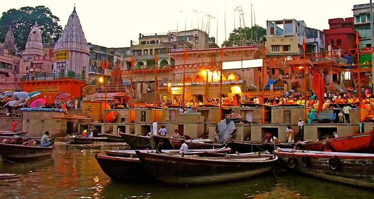 Abendszene der Ghats von Varanasi mit beleuchteten Tempeln, farbenfrohen Gebäuden und Booten auf dem Ganges.