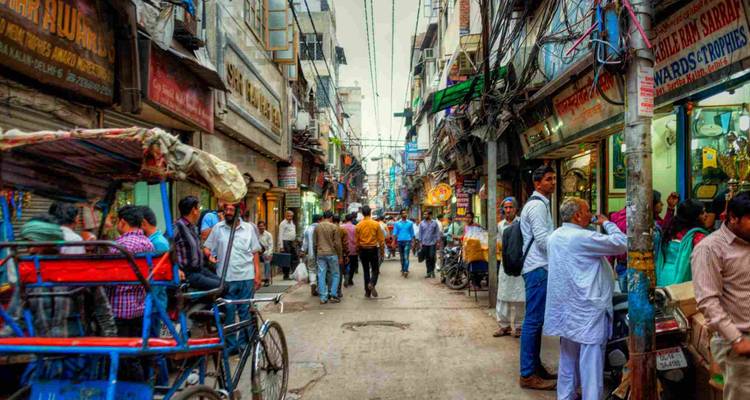 Bunte, überfüllte Marktgasse in Alt-Delhi voller Rikschas, Käufer und hängender Kabel.