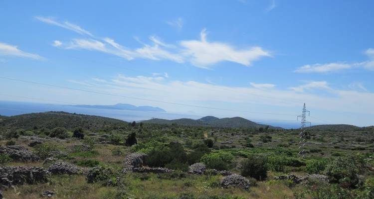 Paisaje montañoso con vegetación dispersa y vista lejana al mar.