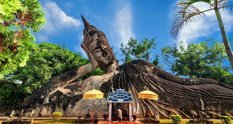 A large reclining Buddha statue in a park setting.