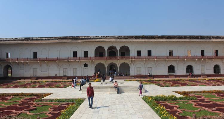 Edificio histórico blanco con personas caminando al frente, jardines bien cuidados.