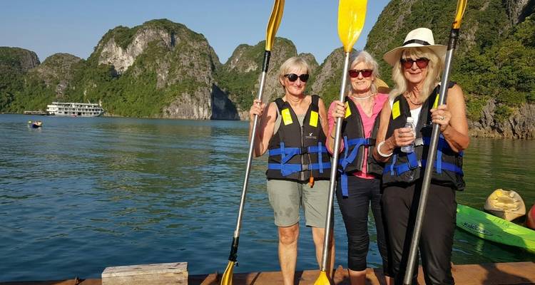 Drie vrouwen poseren met peddels voor een baai met kalkstenen bergen.