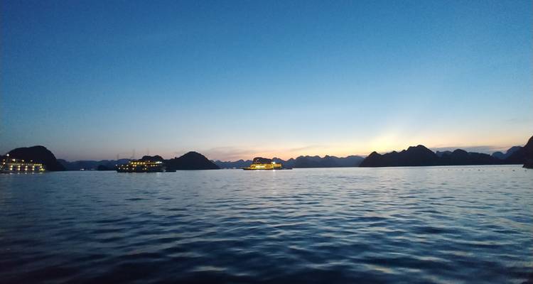 Coucher de soleil sur une baie avec des silhouettes de bateaux à l'horizon.